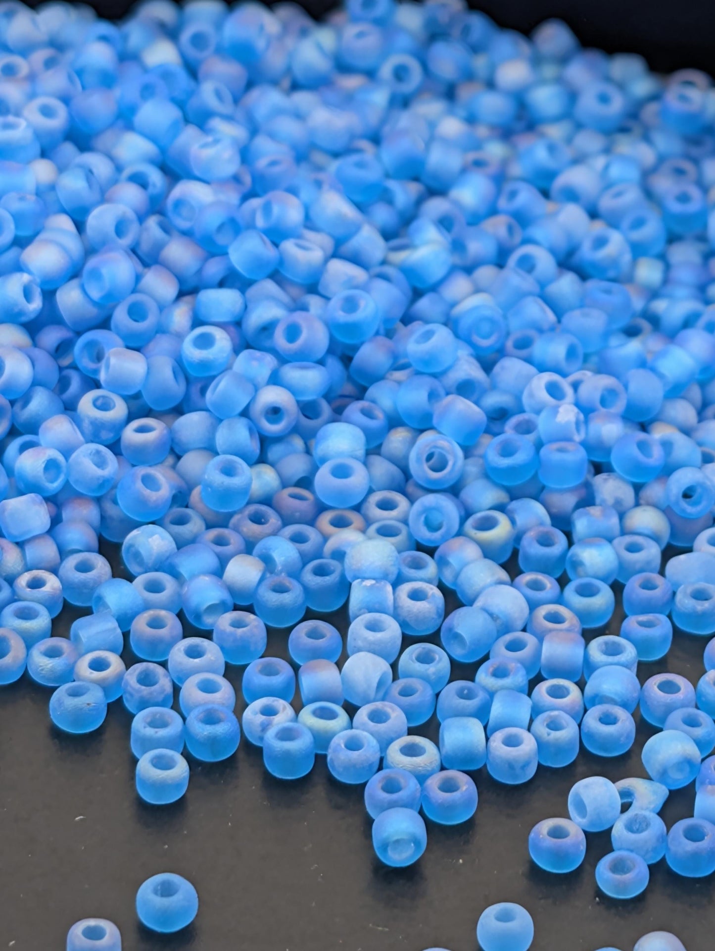 a large pile of small, clear blue beads scattered on a dark surface.