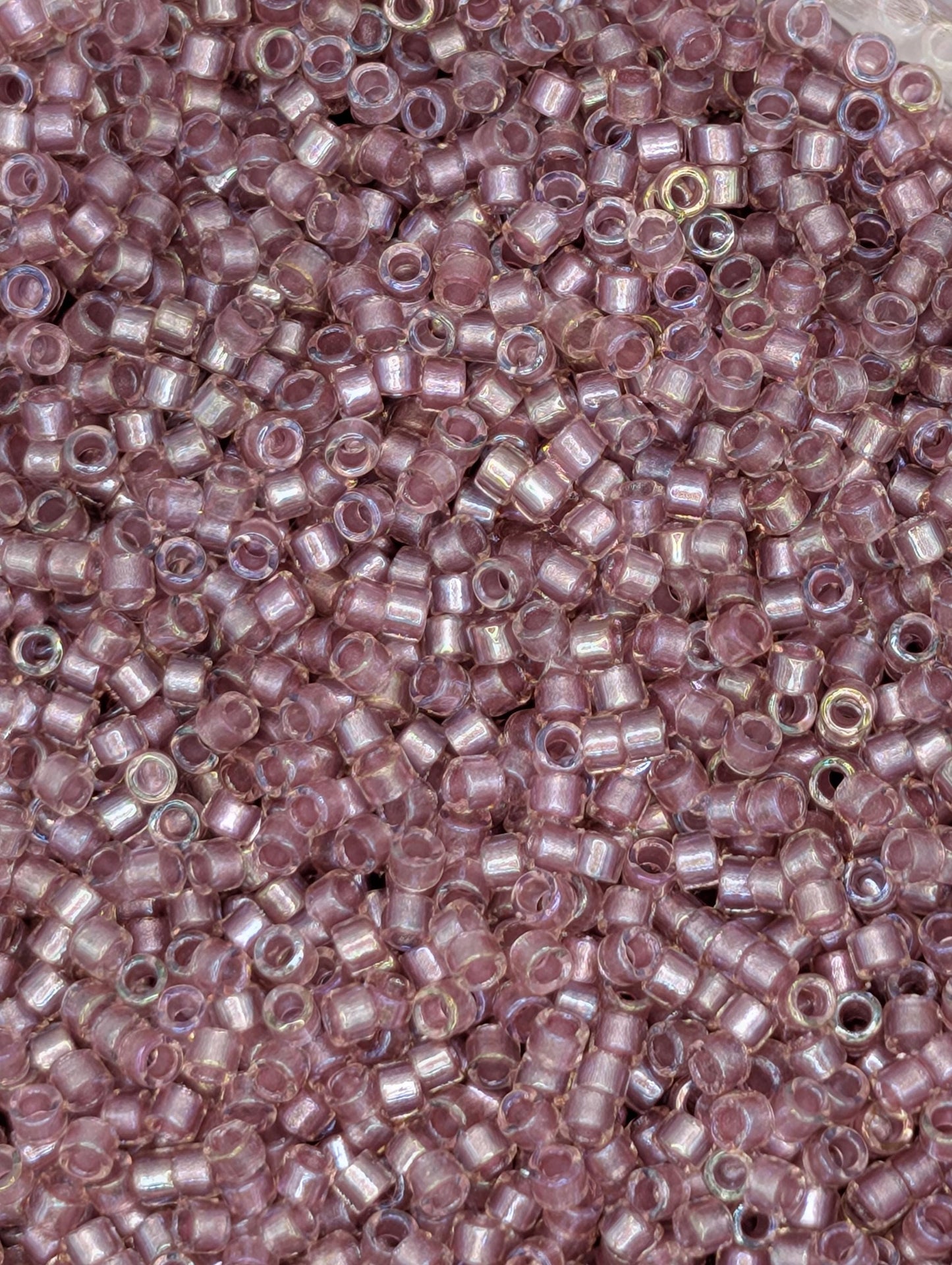 The image is a close-up of numerous small, round beads in shades of pink and purple.