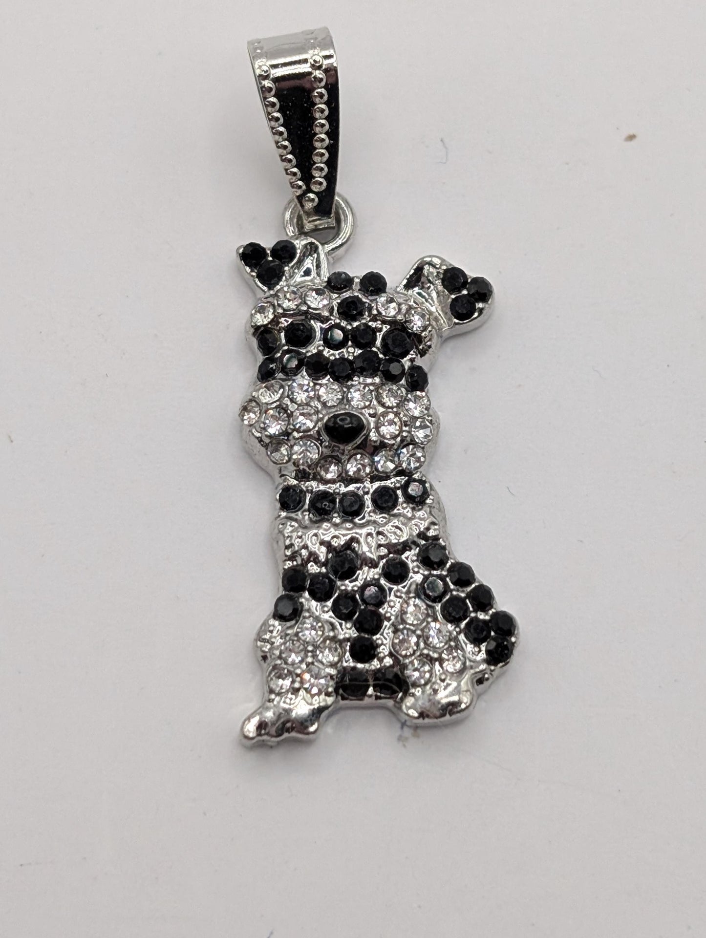 A silver-toned pendant in the shape of a dog, adorned with black and white rhinestones or crystals.