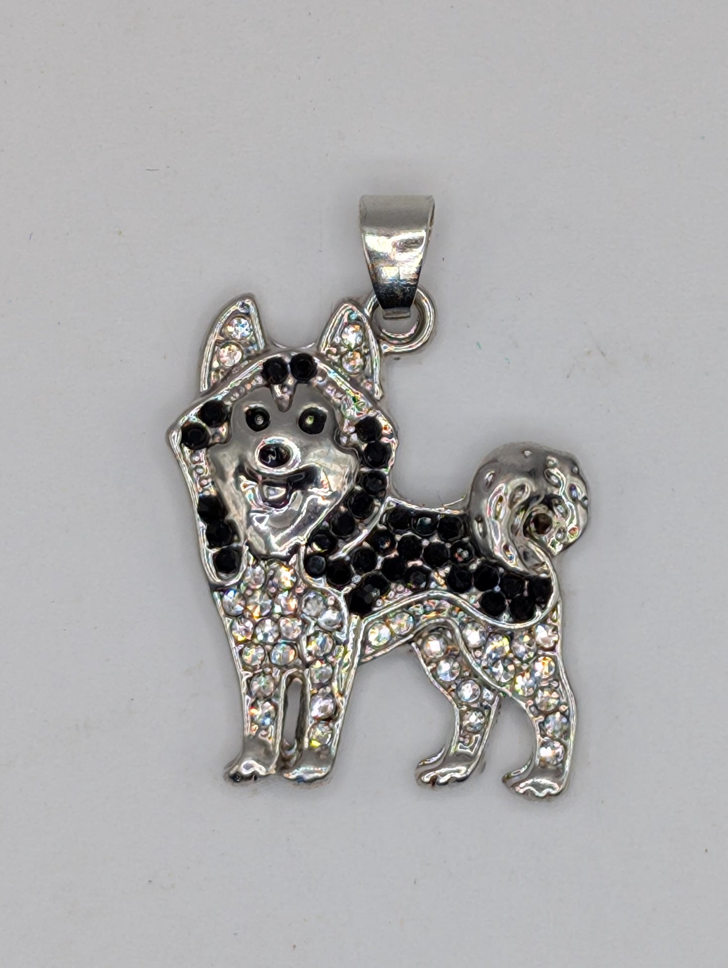 A silver-colored pendant in the shape of a dog, adorned with black and white rhinestones or crystals.