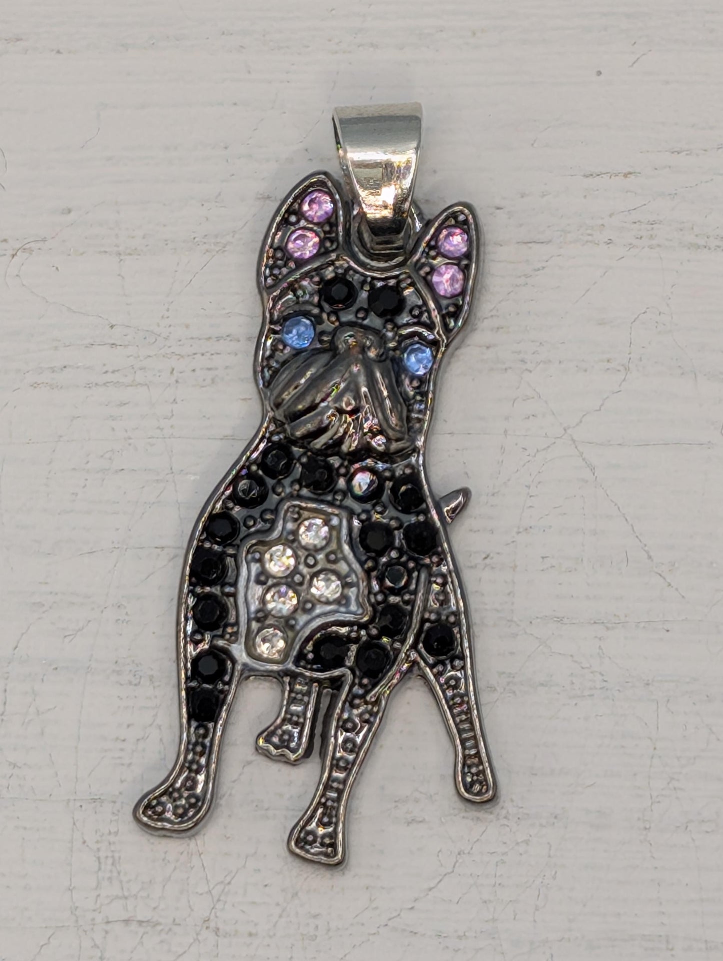 A decorative pendant in the shape of a dog, with a metallic appearance and adorned with small gemstones or crystals.