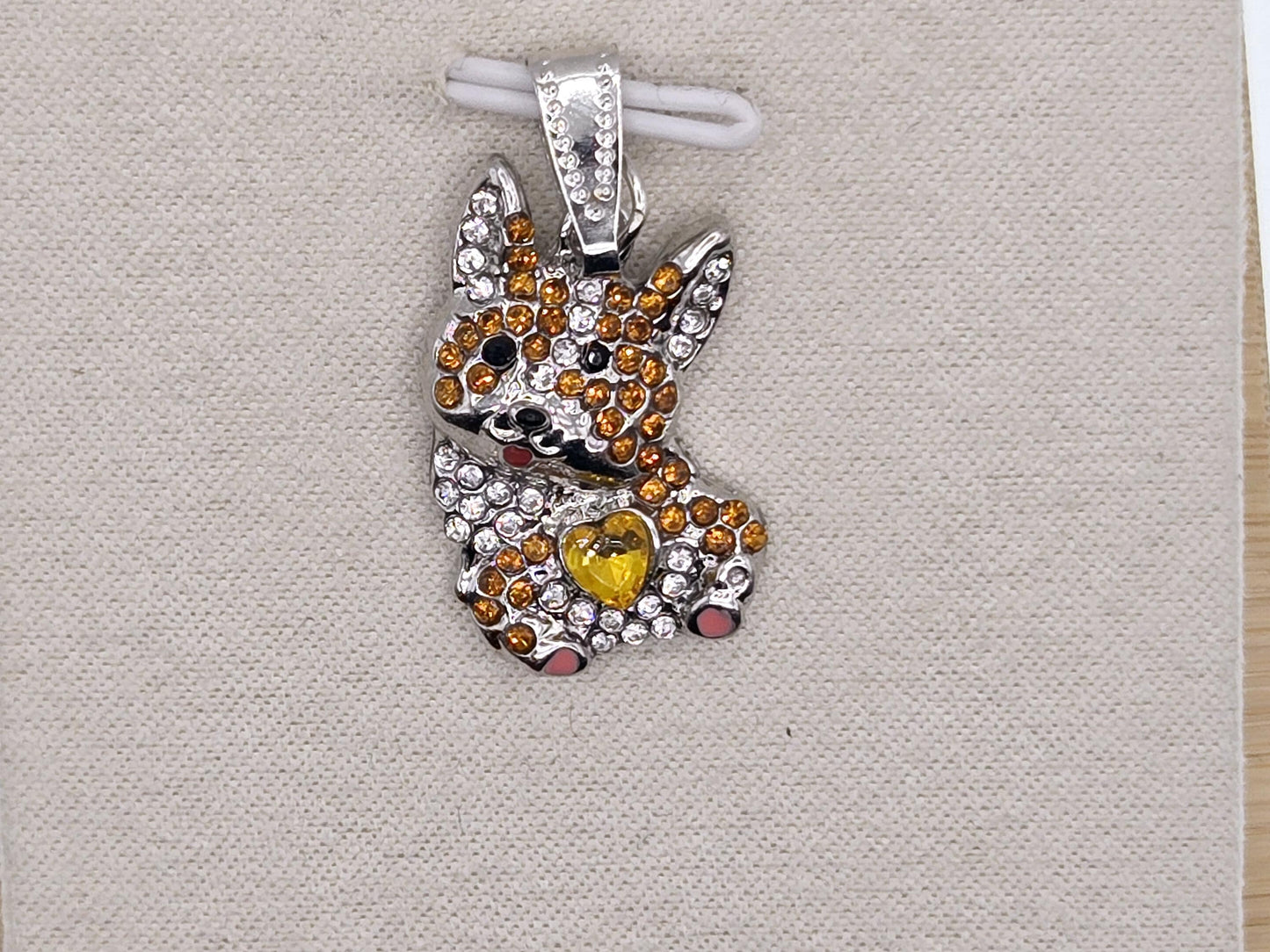 A silver-colored pendant in the shape of a dog, adorned with colorful gemstones and a heart-shaped gemstone.
