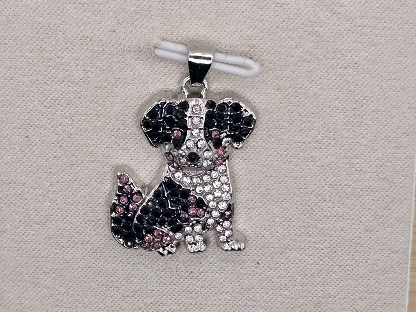 A silver-toned pendant in the shape of a dog, adorned with sparkling rhinestones and colored gemstones.