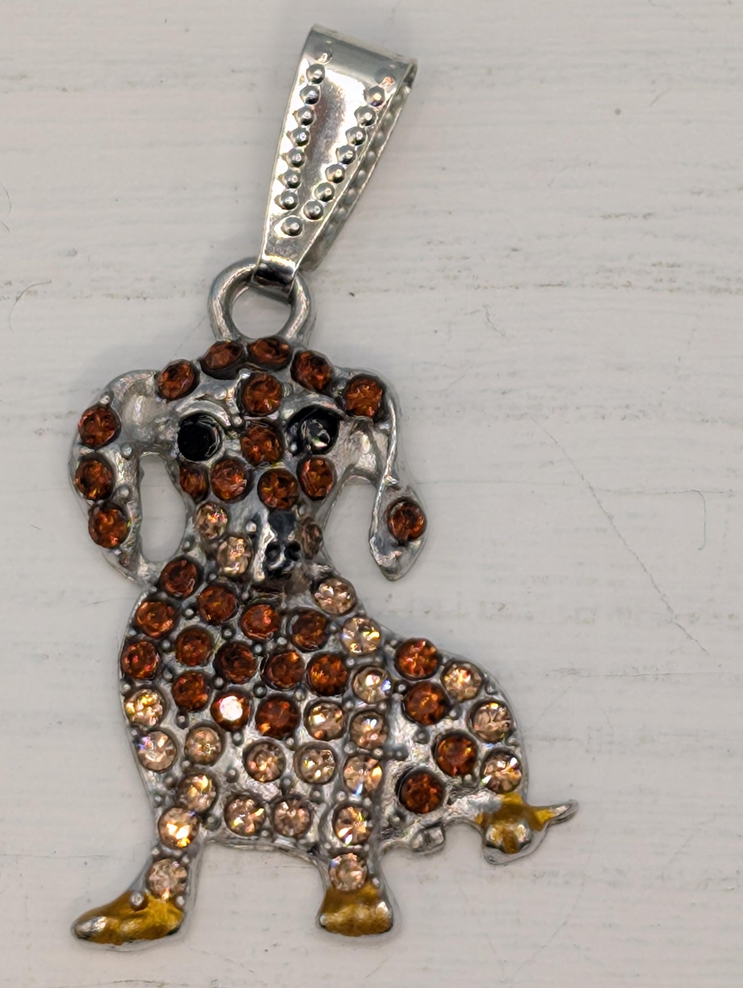 A decorative pendant in the shape of a dog, adorned with numerous small, round, and brown gemstones.