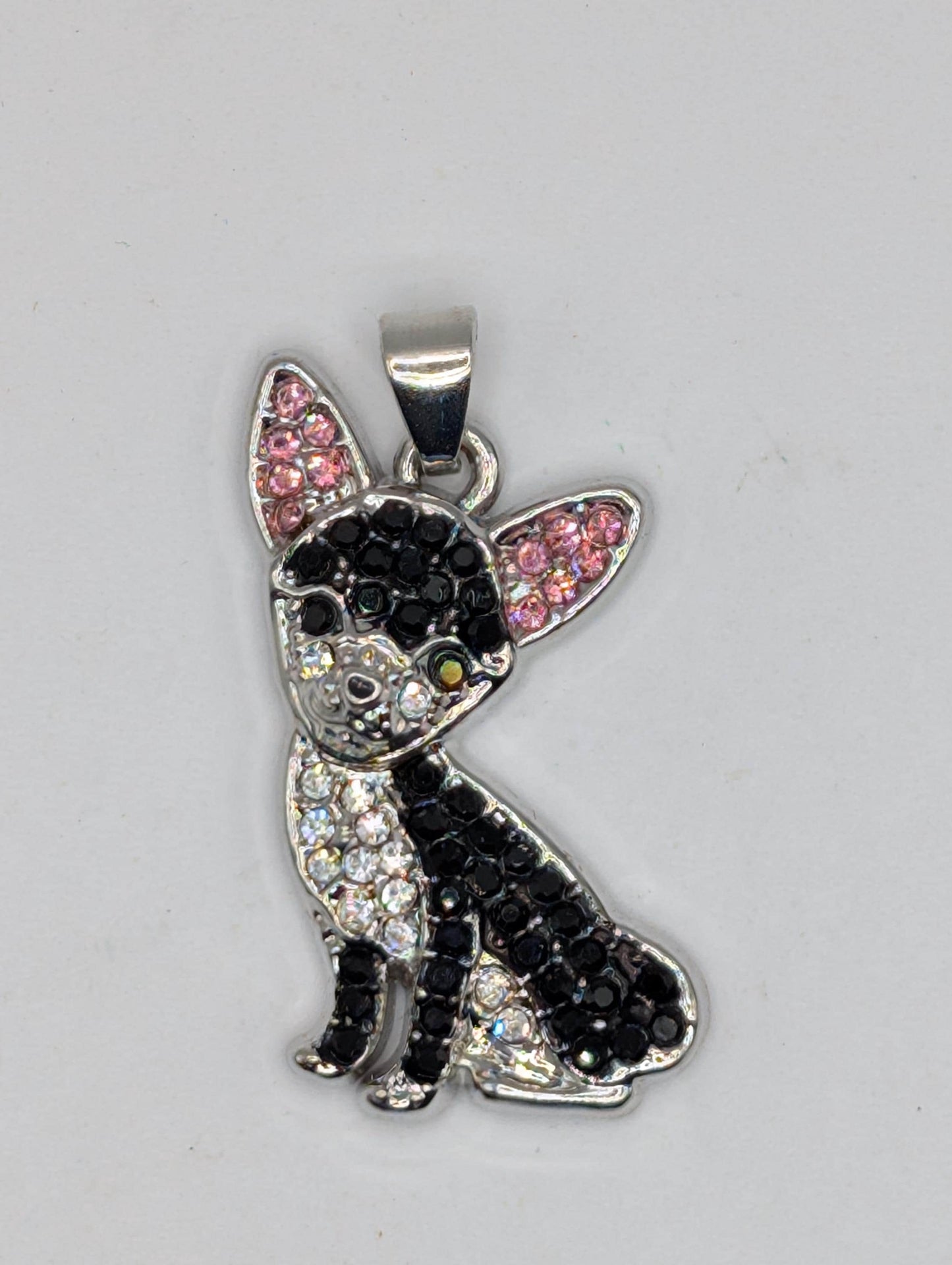 A silver-colored pendant in the shape of a dog, adorned with black and pink rhinestones or crystals.
