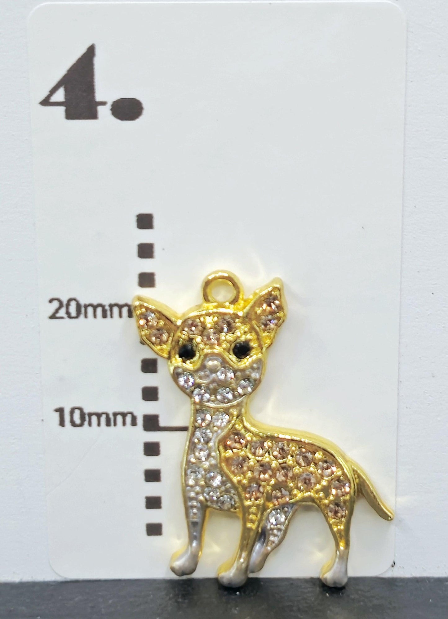 A gold-colored charm in the shape of a dog, adorned with rhinestones or crystals, is displayed against a white background.