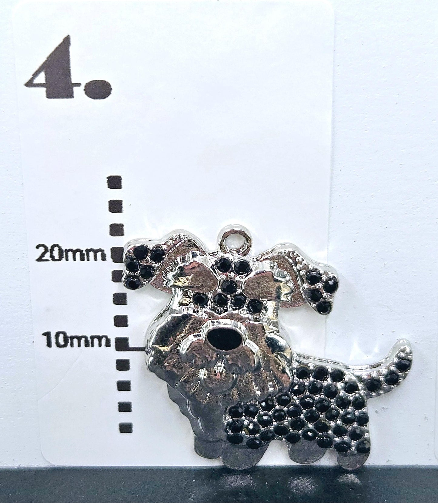 A silver charm in the shape of a dog, adorned with black rhinestones, is displayed against a white background.