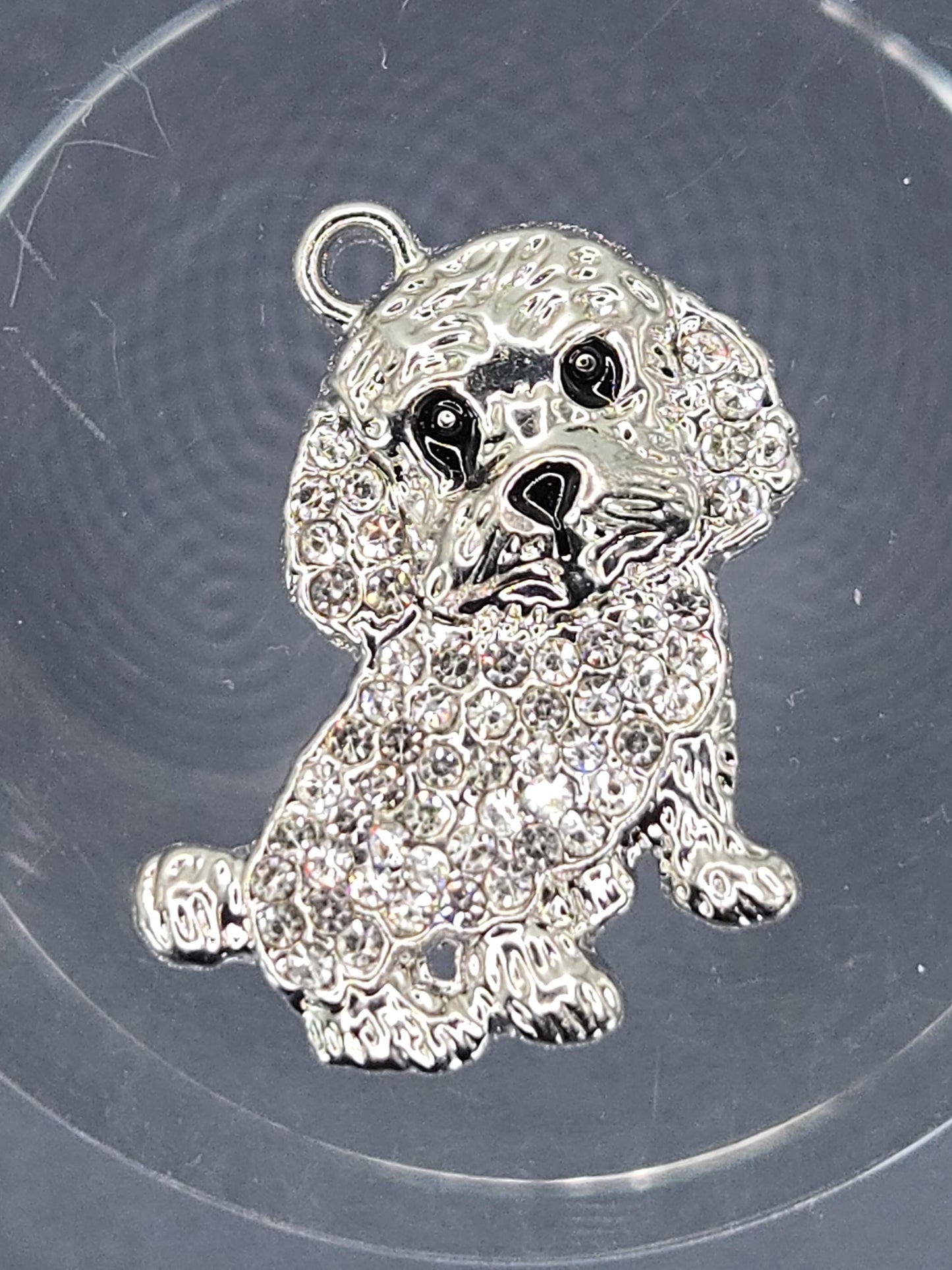 A silver-colored charm in the shape of a dog, adorned with sparkling rhinestones or crystals.