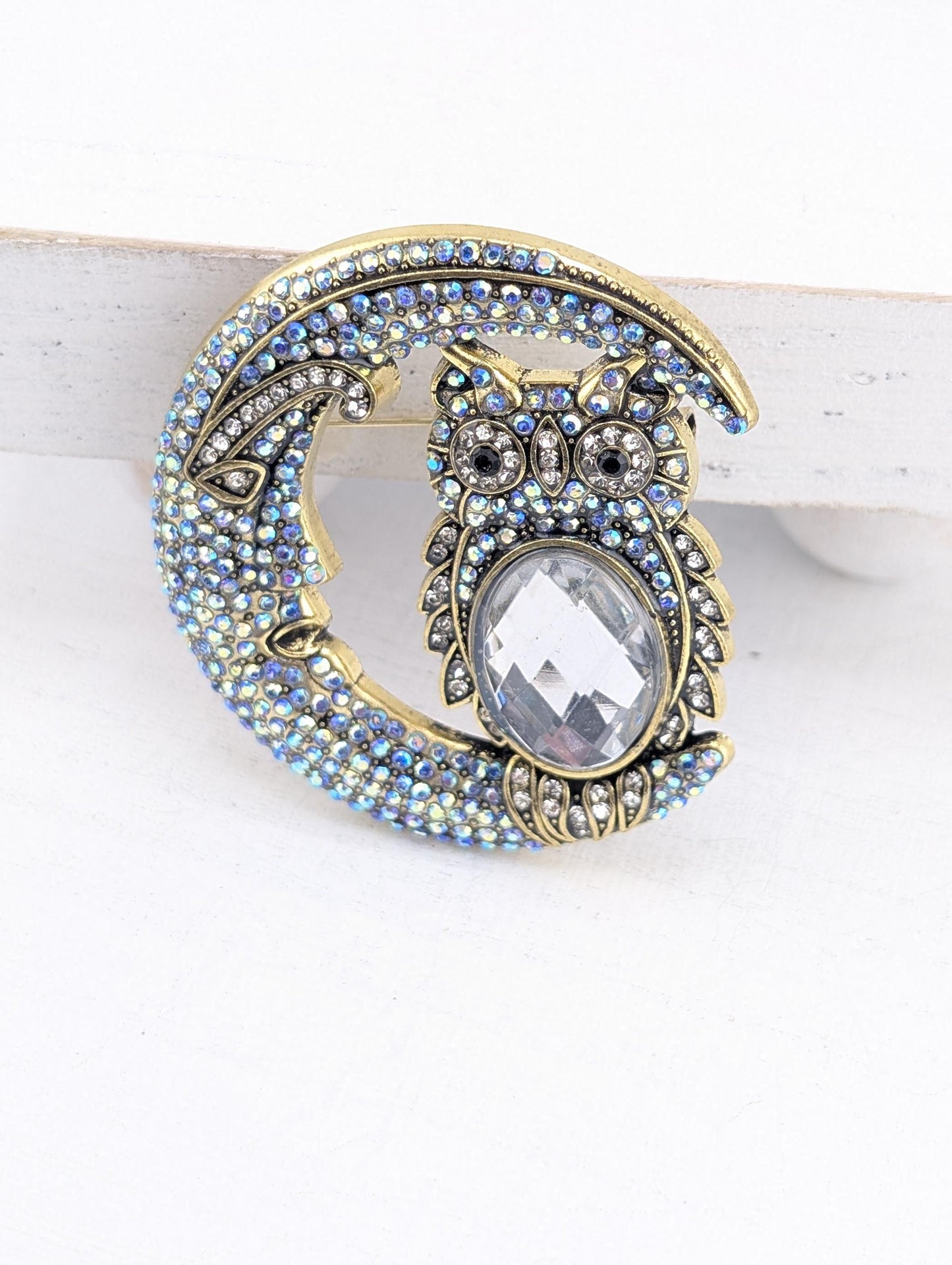 A decorative brooch in the shape of a crescent moon, adorned with blue and white gemstones and a large clear gemstone in the center.