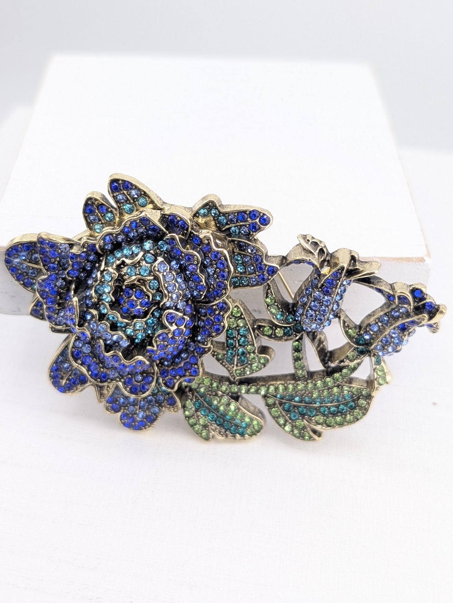 A decorative piece featuring a large blue flower with green leaves and sparkling gemstones.