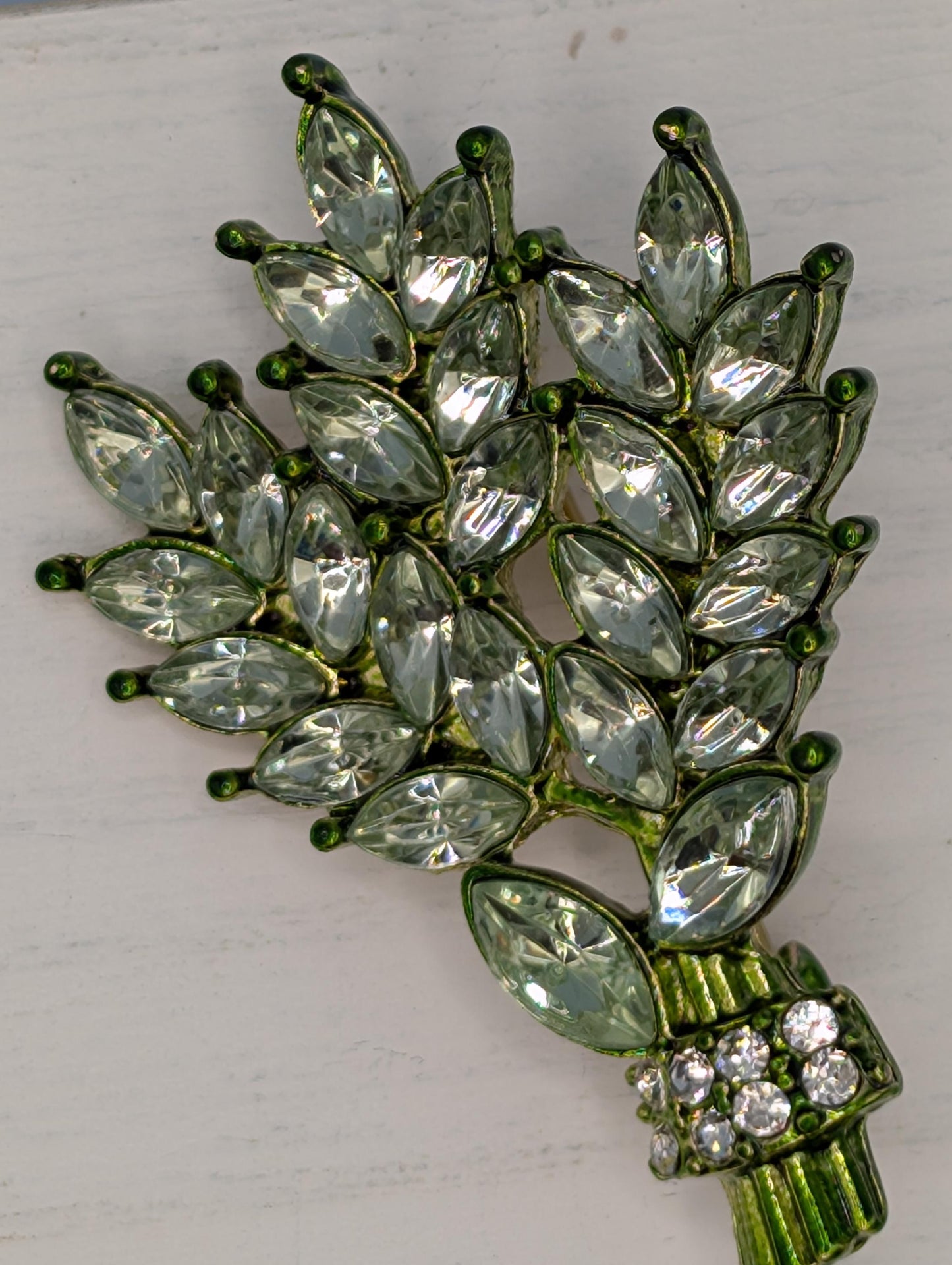 A decorative brooch with a leaf-like design, featuring numerous small, clear gemstones in various shapes and sizes.