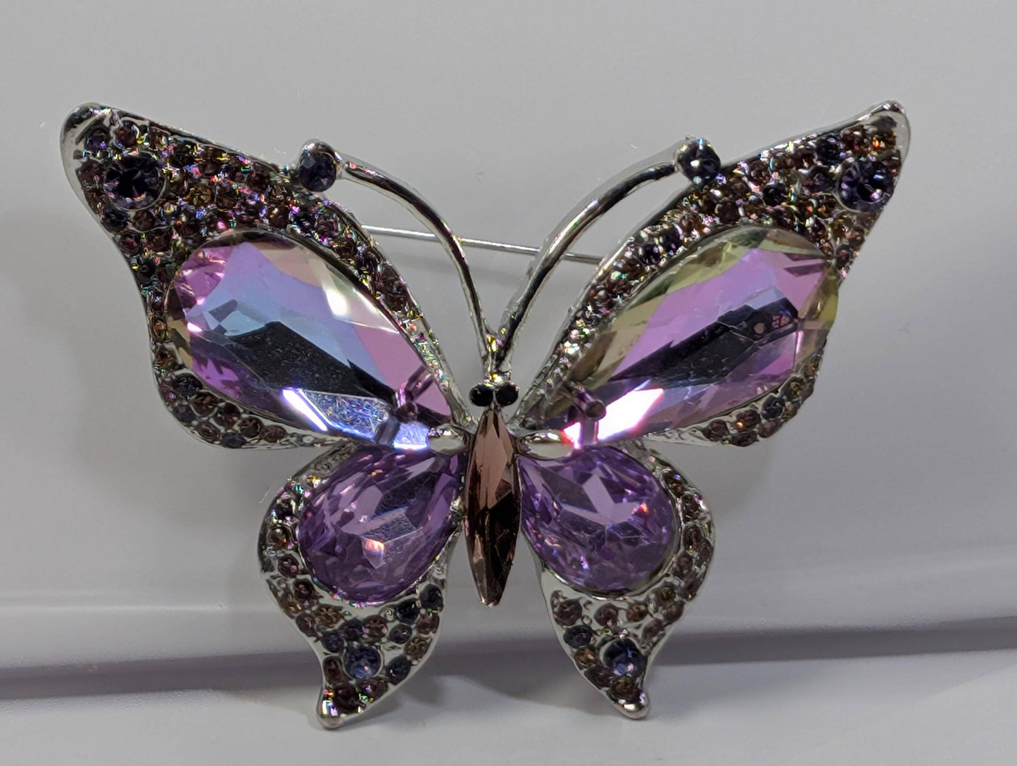 A silver pin in the shape of a butterfly, adorned with large purple gemstones.