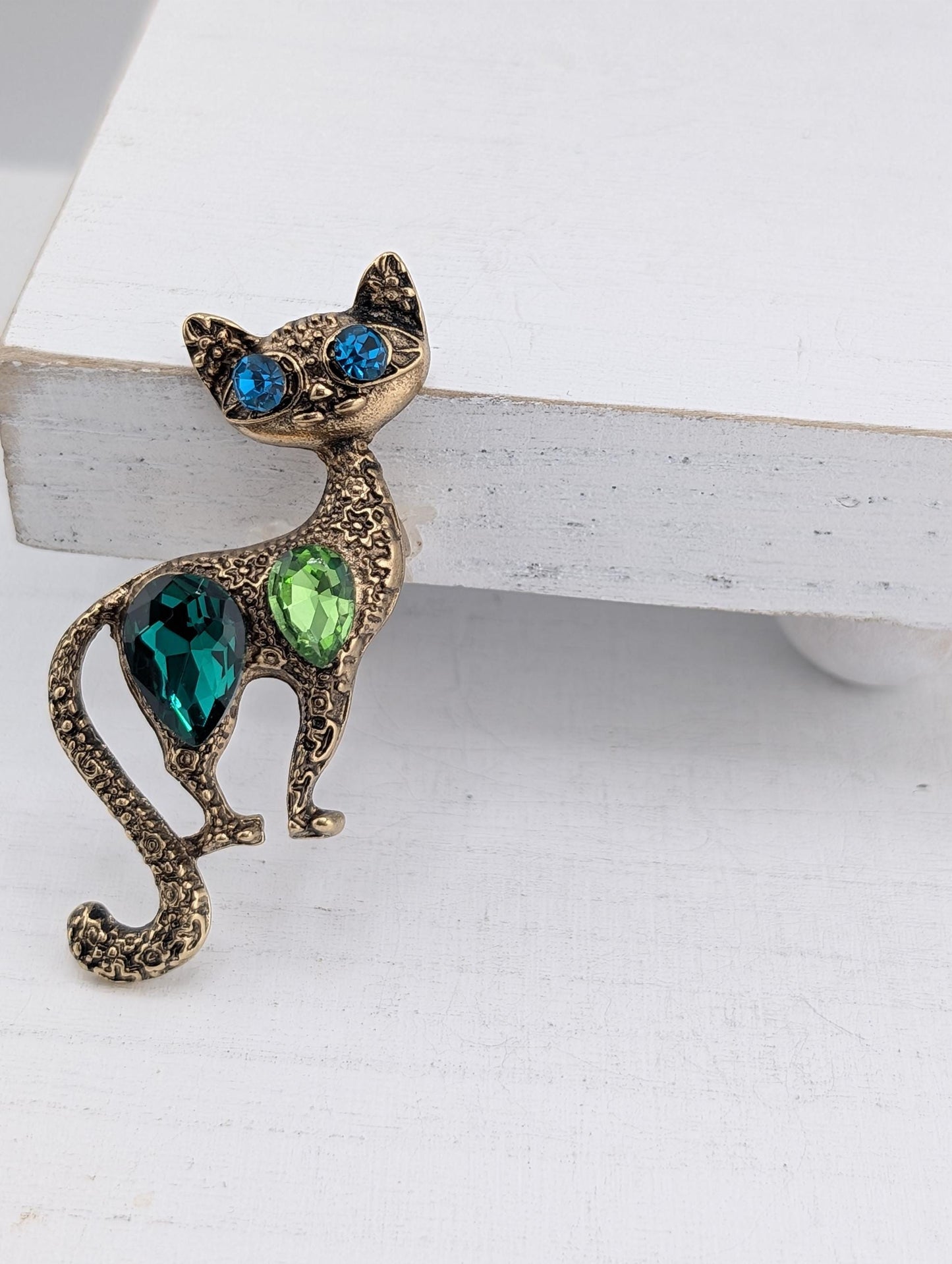 A decorative cat brooch with a gold-colored body and green and blue gemstones on its back.