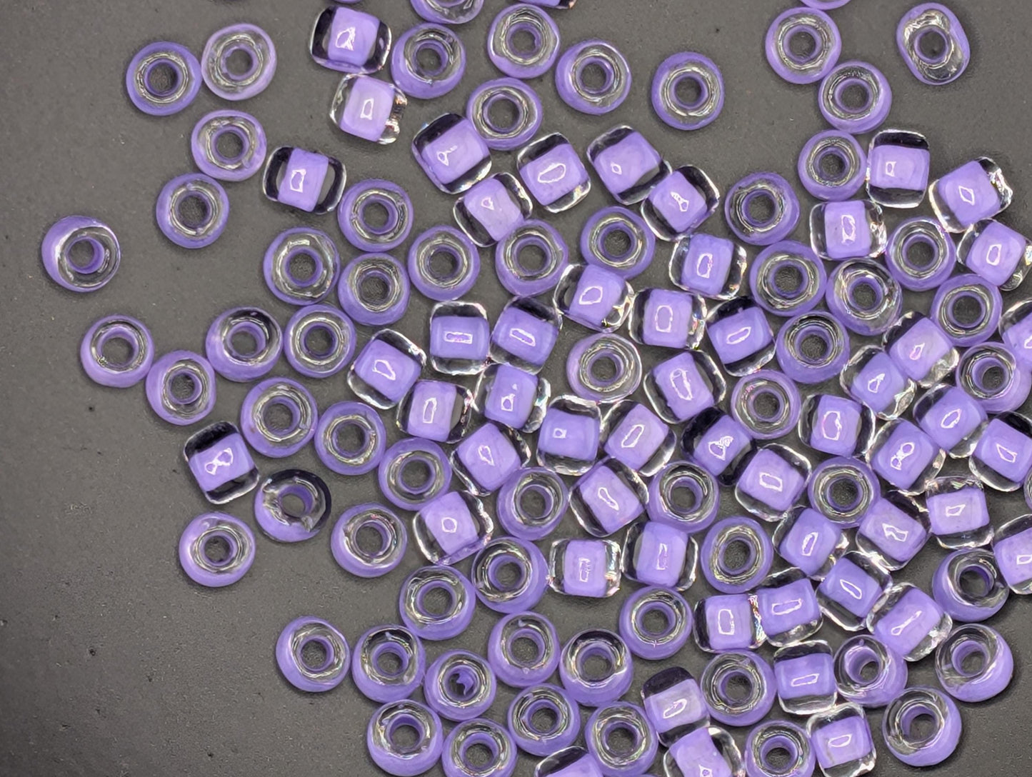a collection of small, clear beads in various shades of purple scattered across a gray surface.