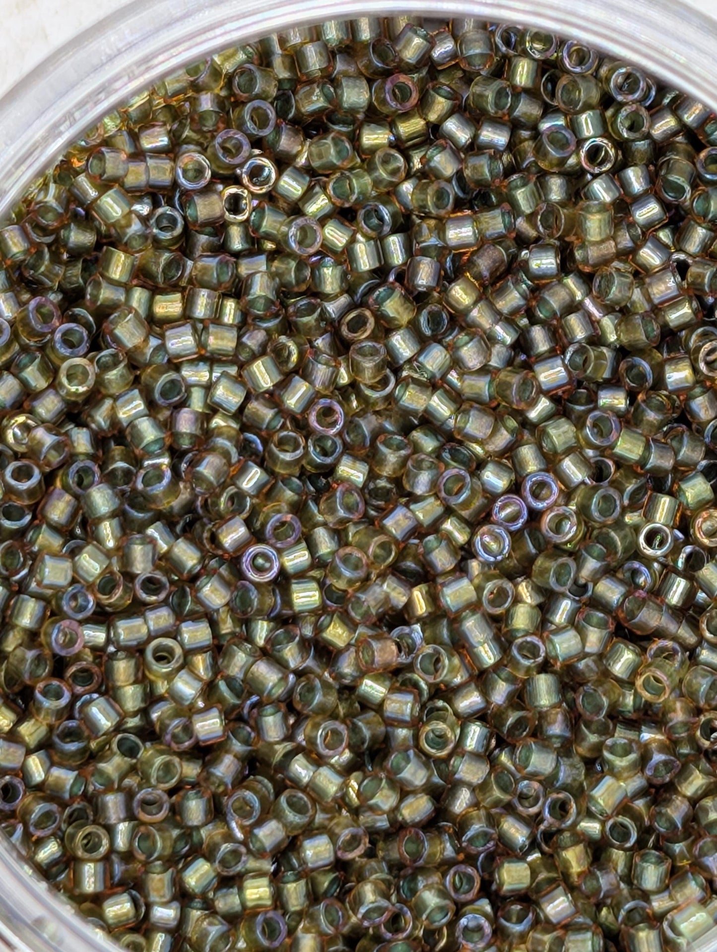 A close-up image of a container filled with numerous small, round beads in various shades of green and brown.