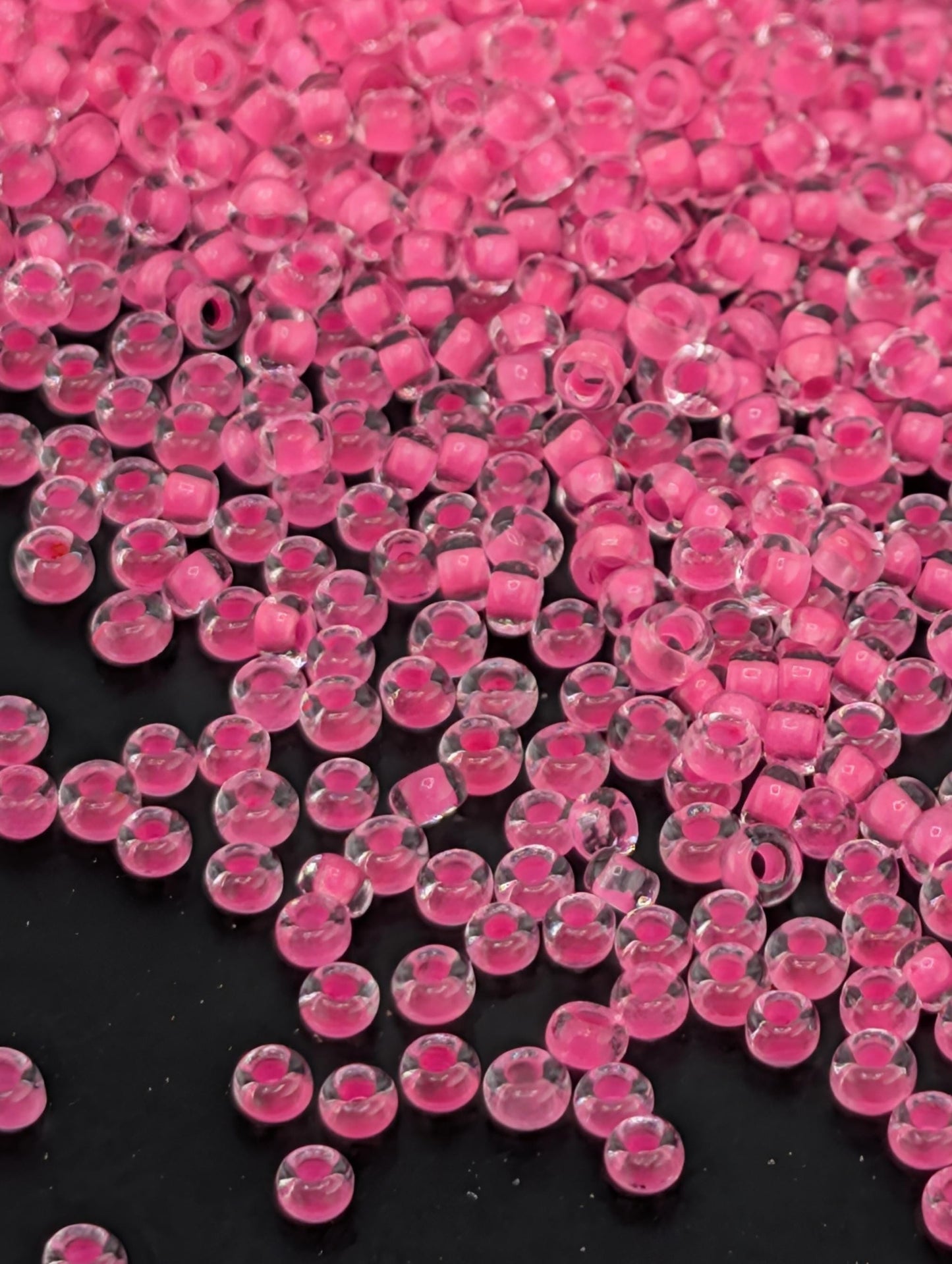 The image is a close-up of numerous small, clear beads in a vibrant shade of pink, scattered across a dark background.