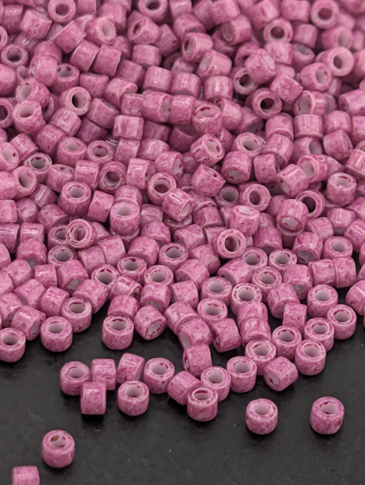 a large pile of small, pink beads scattered on a dark surface.