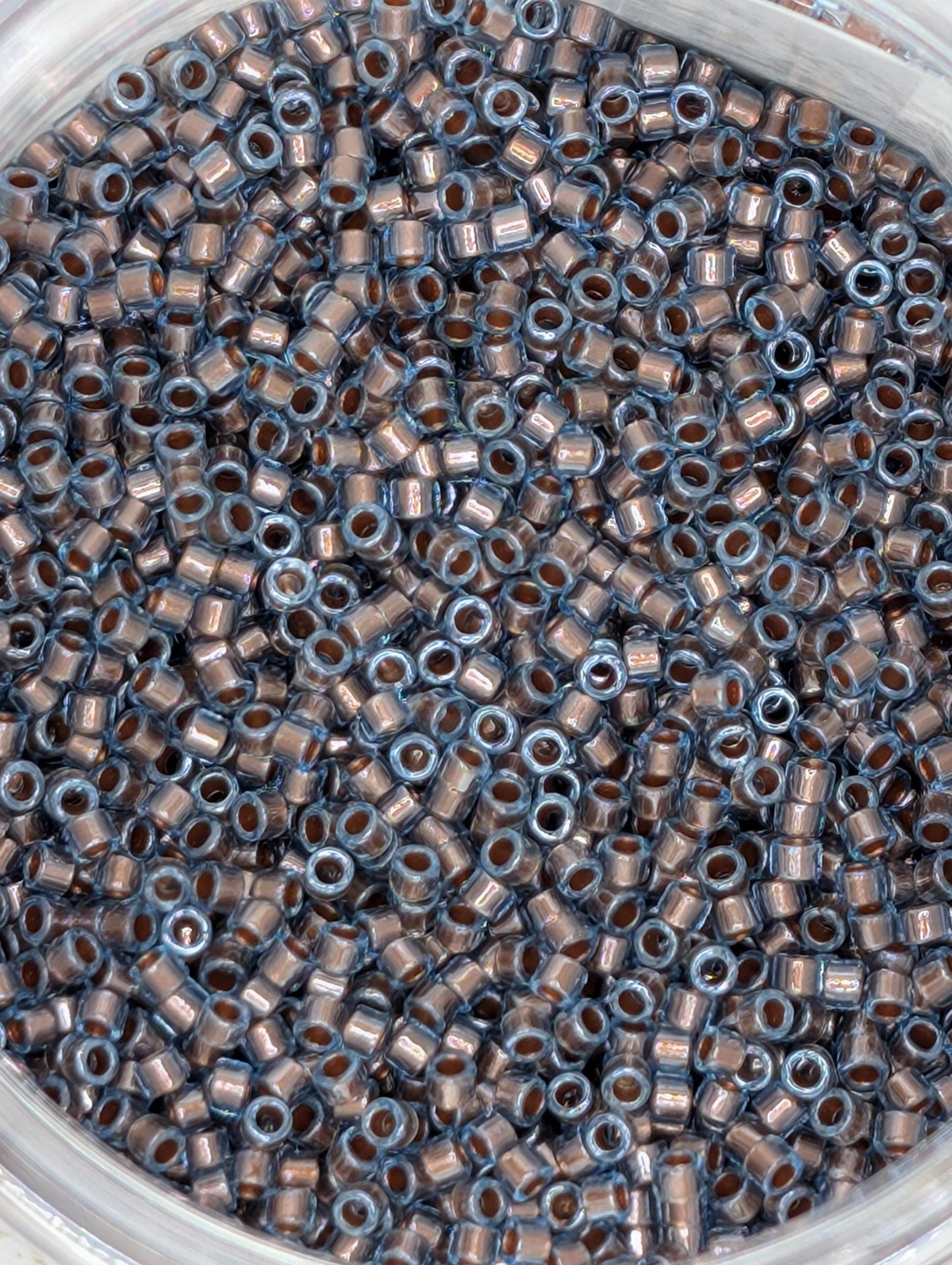 A close-up image of a container filled with numerous small, circular beads in various shades of blue and brown.