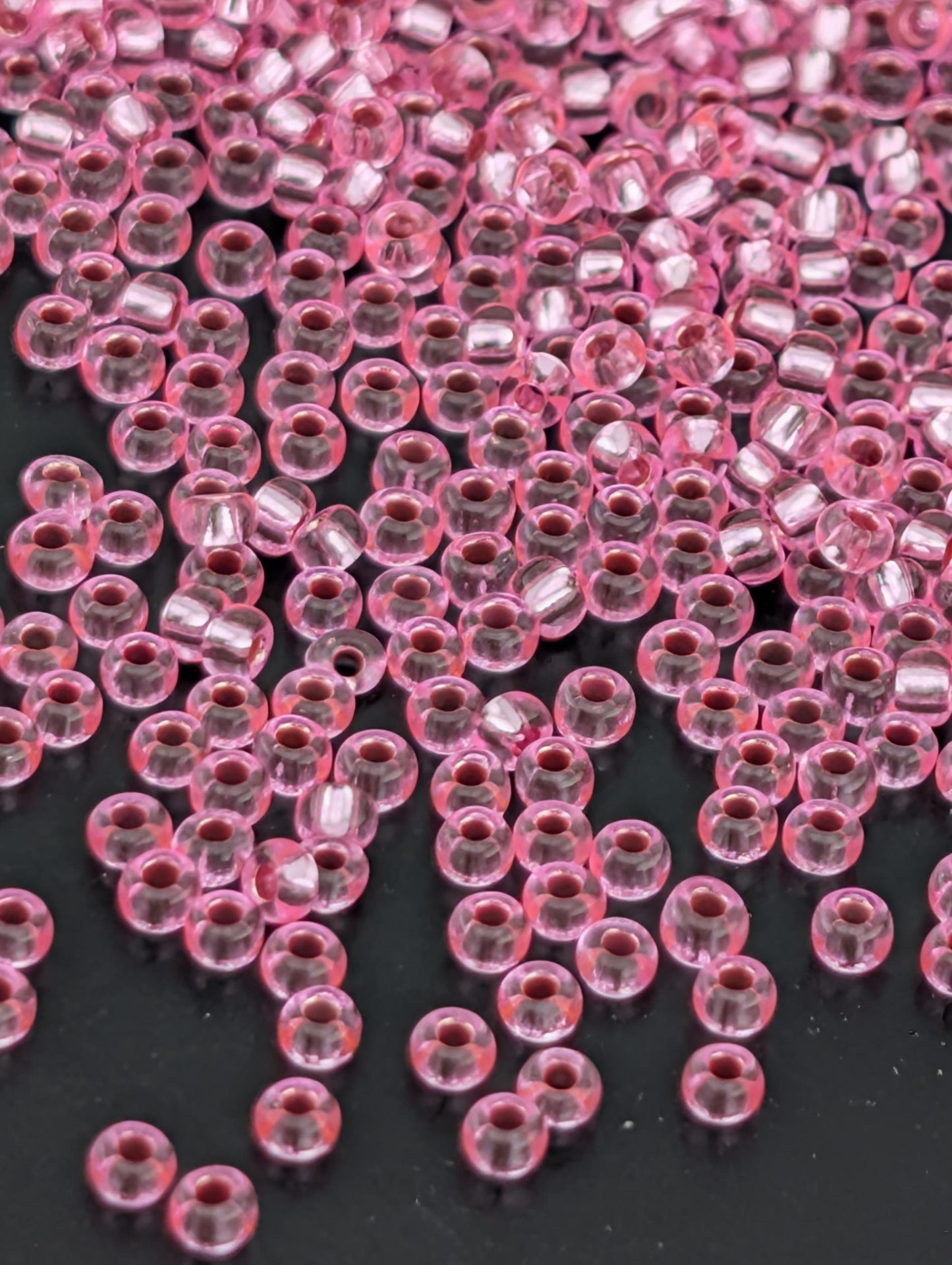 a close-up view of numerous small, clear beads in a pink color, scattered across a dark background.