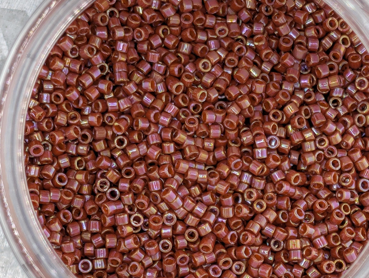 A close-up image of a glass jar filled with numerous small, round beads in a reddish-brown color.