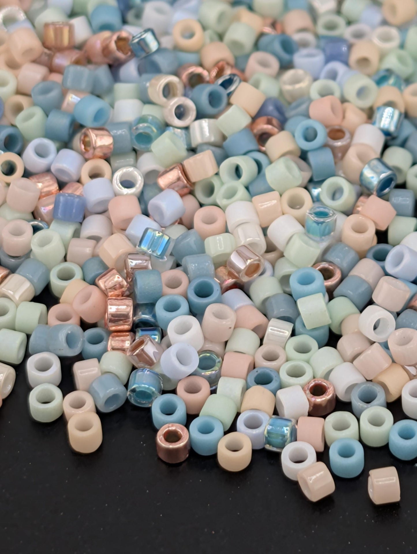 A colorful pile of multicolored beads, including various shades of blue, pink, and white, scattered on a dark surface.