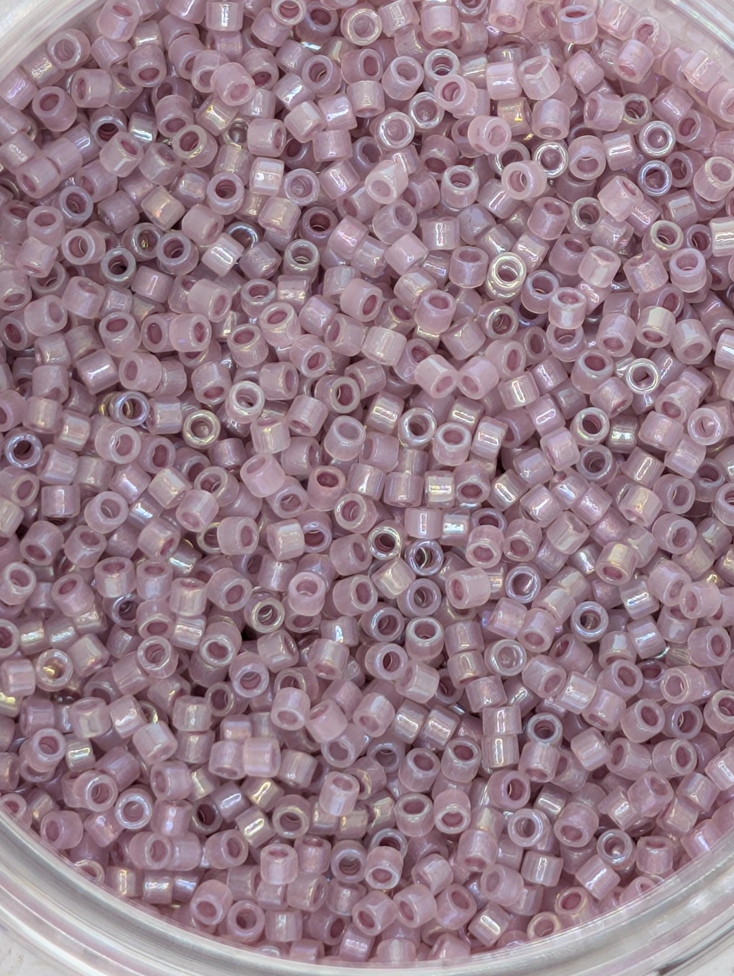 A close-up image of a container filled with numerous small, round beads in a soft, pastel pink color.