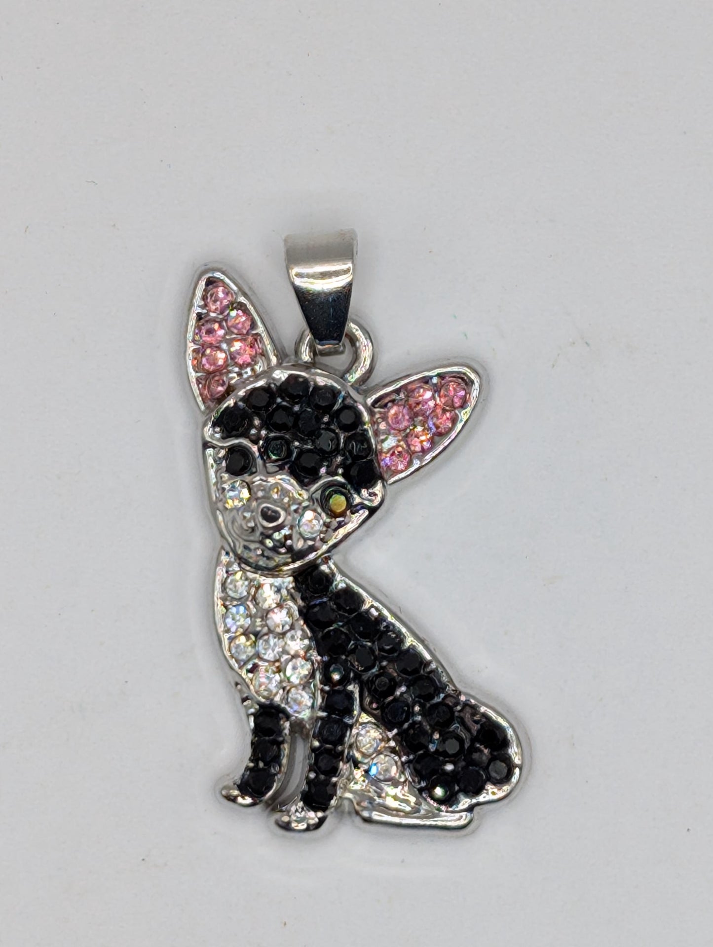 A silver-colored pendant in the shape of a dog, adorned with black and pink rhinestones or crystals.