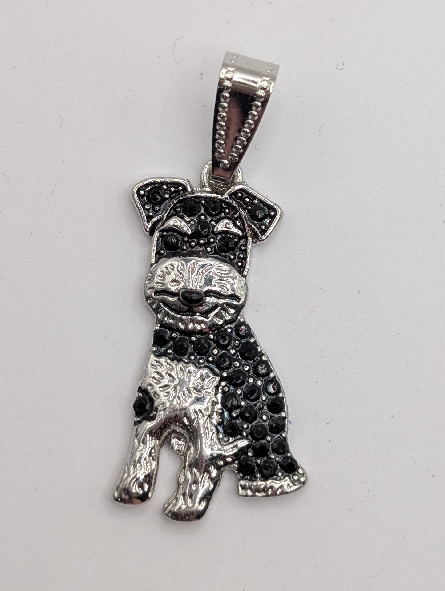 A silver-colored pendant in the shape of a dog, with black rhinestones or crystals adorning it.