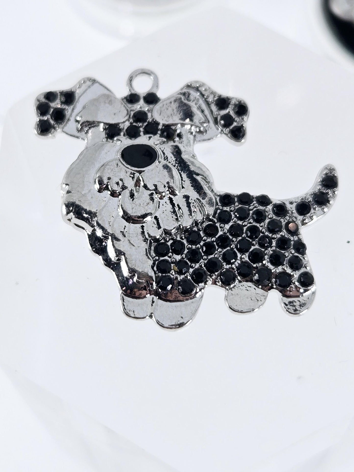 A close-up image of a silver-colored metal charm or pendant with a black diamond-like pattern covering its surface.