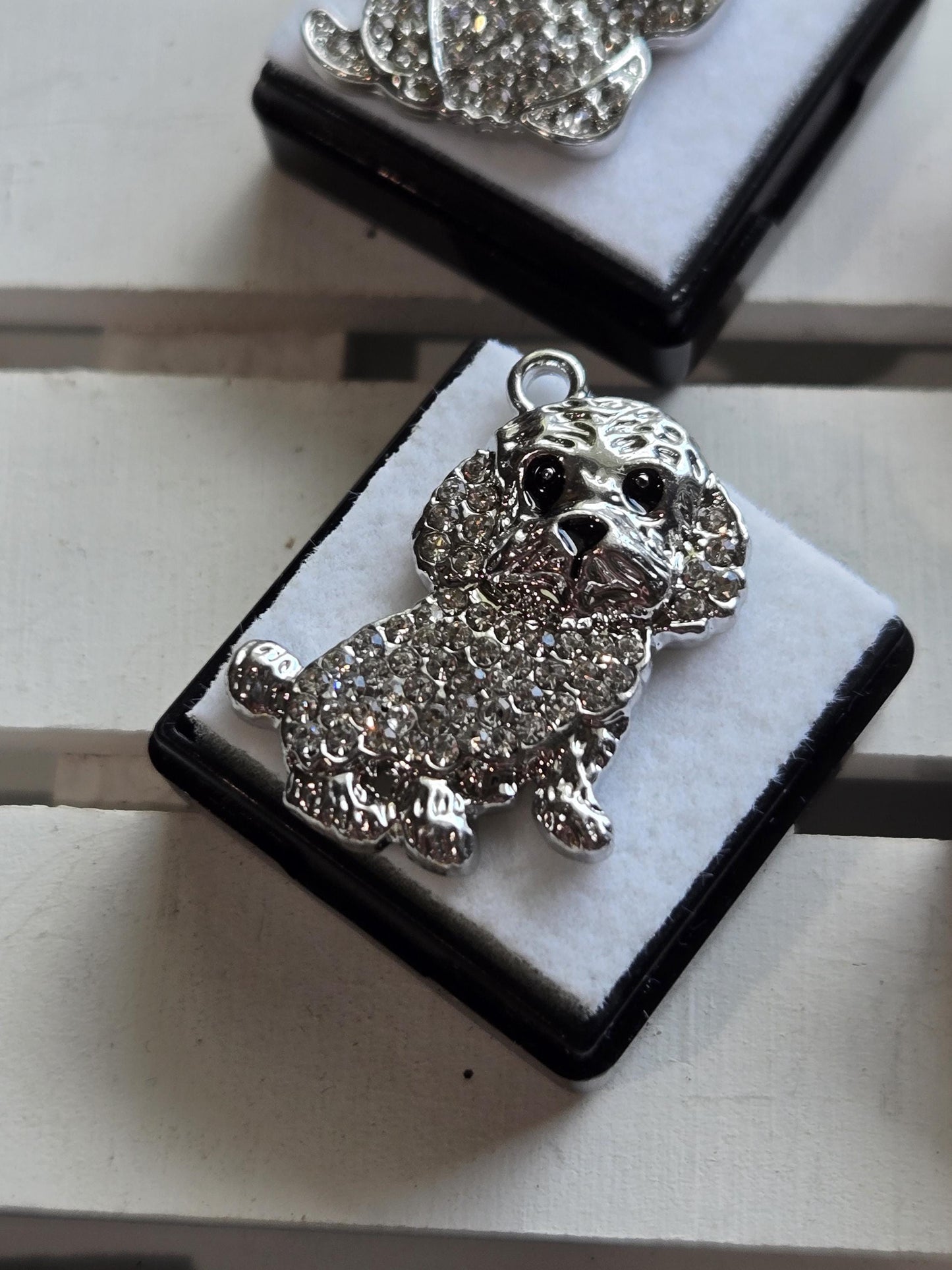A close-up image of a silver poodle charm or brooch with a sparkling crystal design.