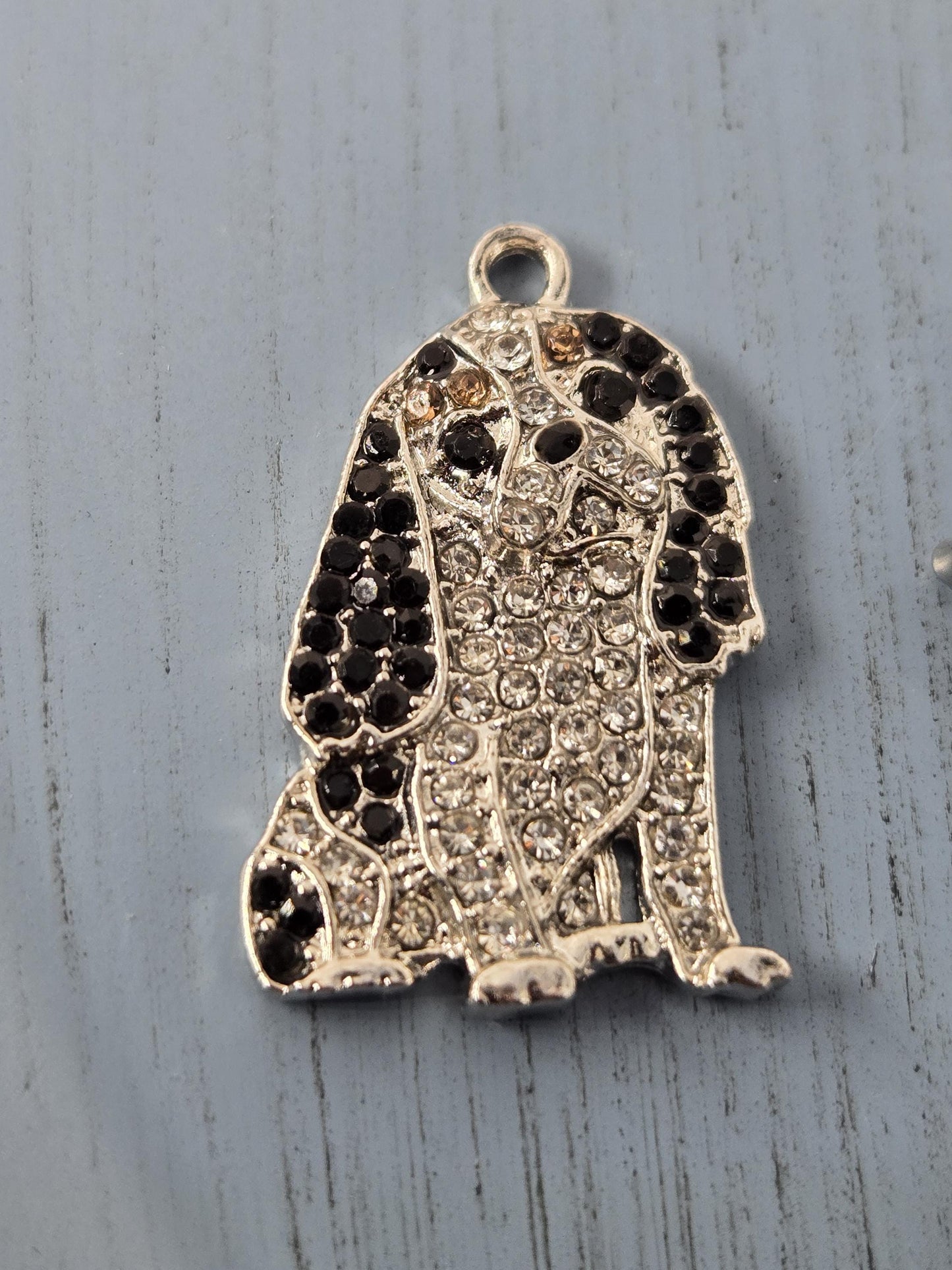 A silver-colored charm in the shape of a dog, adorned with numerous small diamonds.