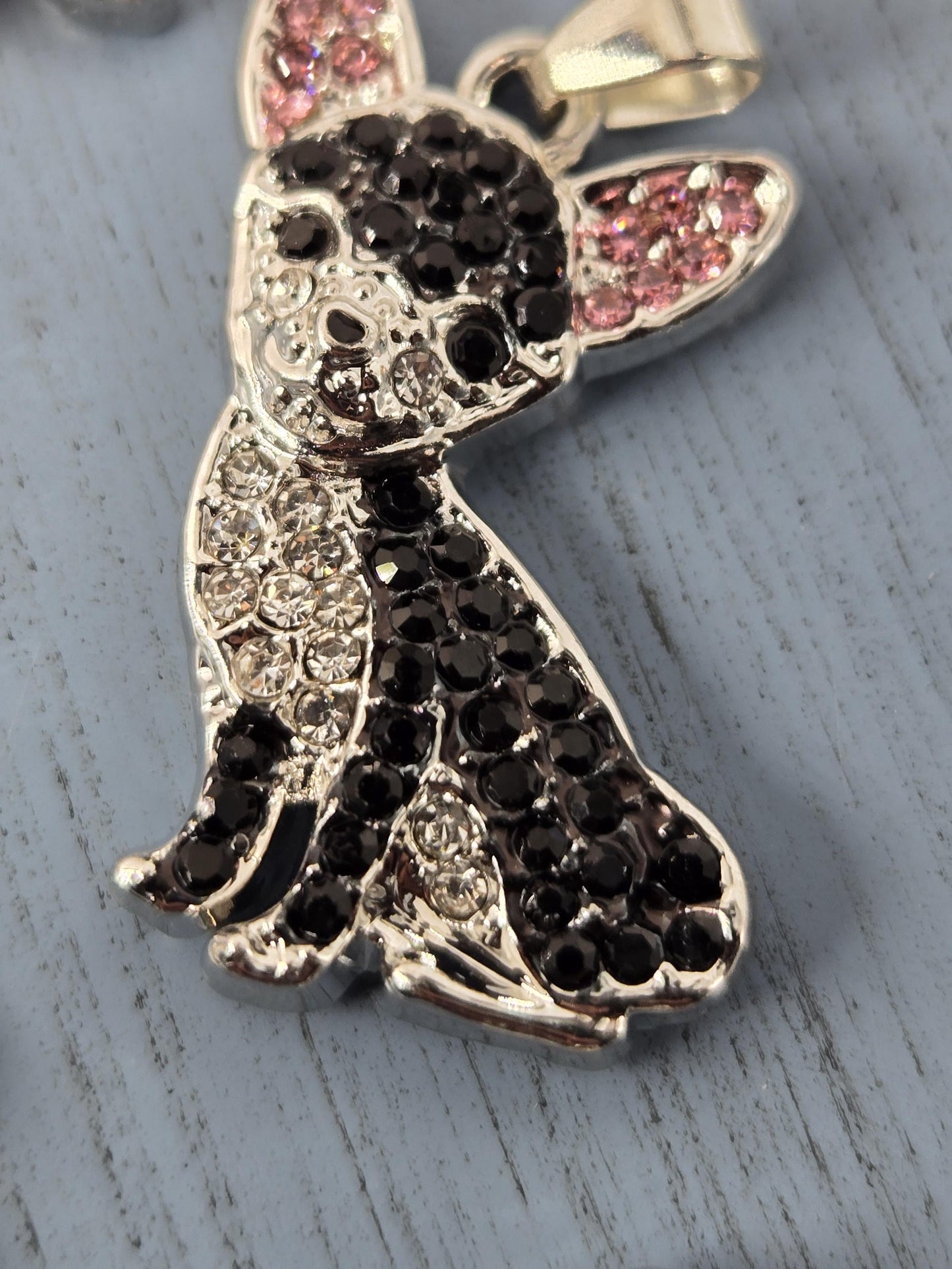 A close-up image of a decorative pendant featuring a stylized design of a bird or bird-like figure, with a combination of black and pink gemstones or crystals adorning the piece.