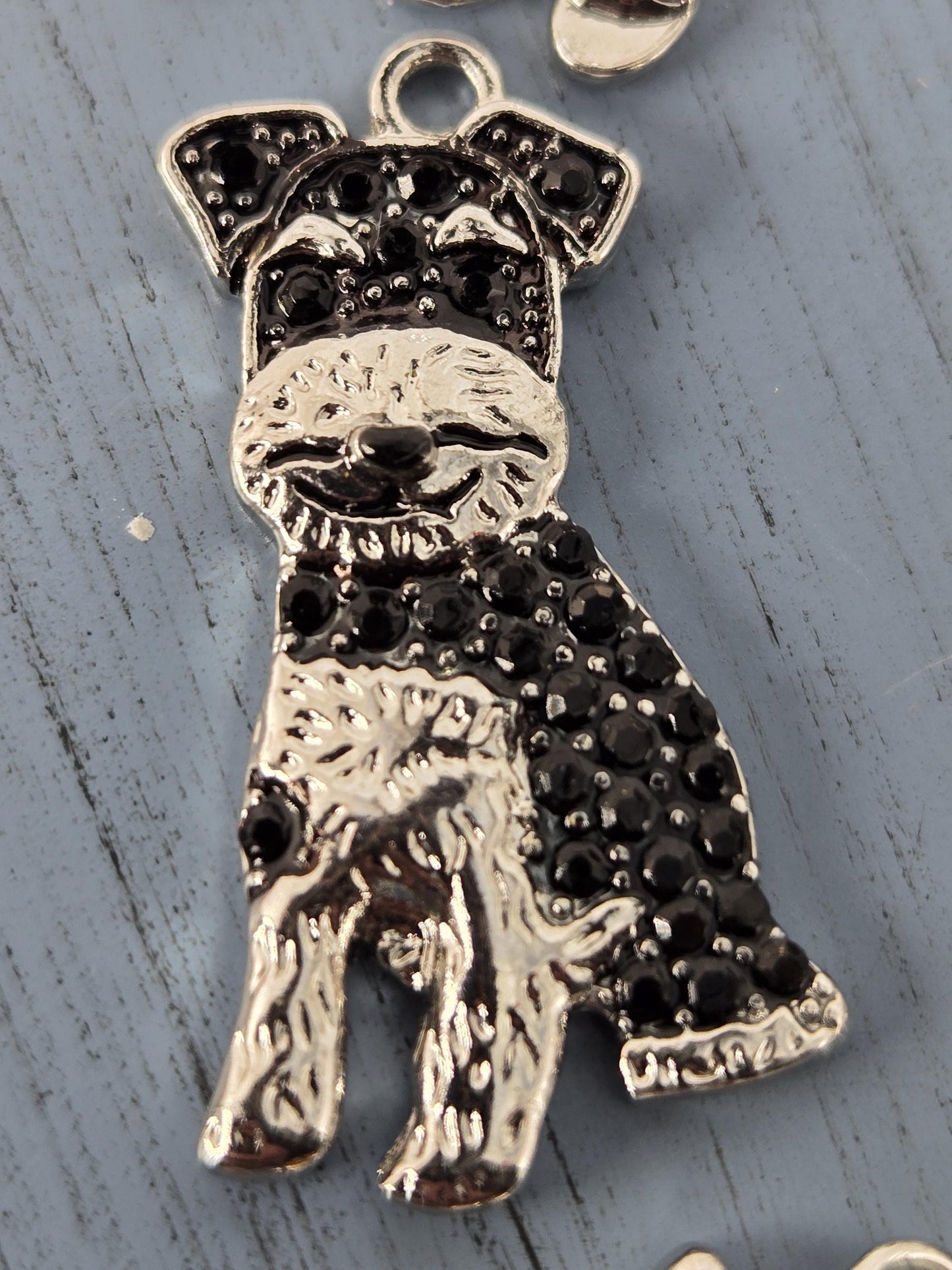 A close-up image of a decorative metal charm in the shape of a dog, with black gemstones or stones embedded in it.
