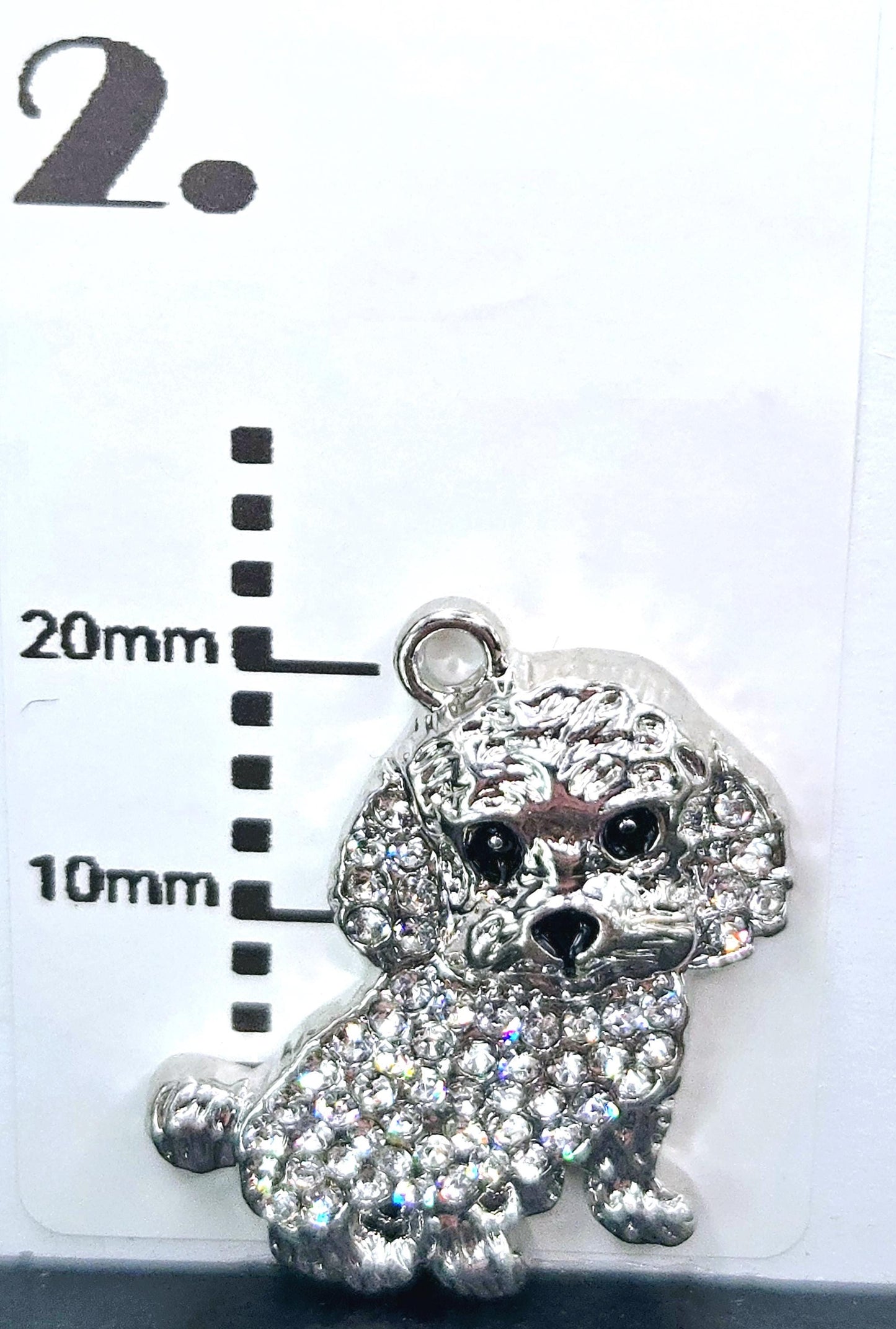 A silver charm in the shape of a poodle, adorned with rhinestones, is displayed against a white background.