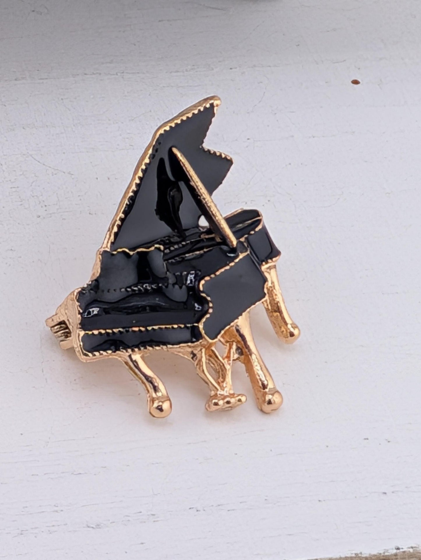 A black and gold piano brooch is displayed on a white surface.