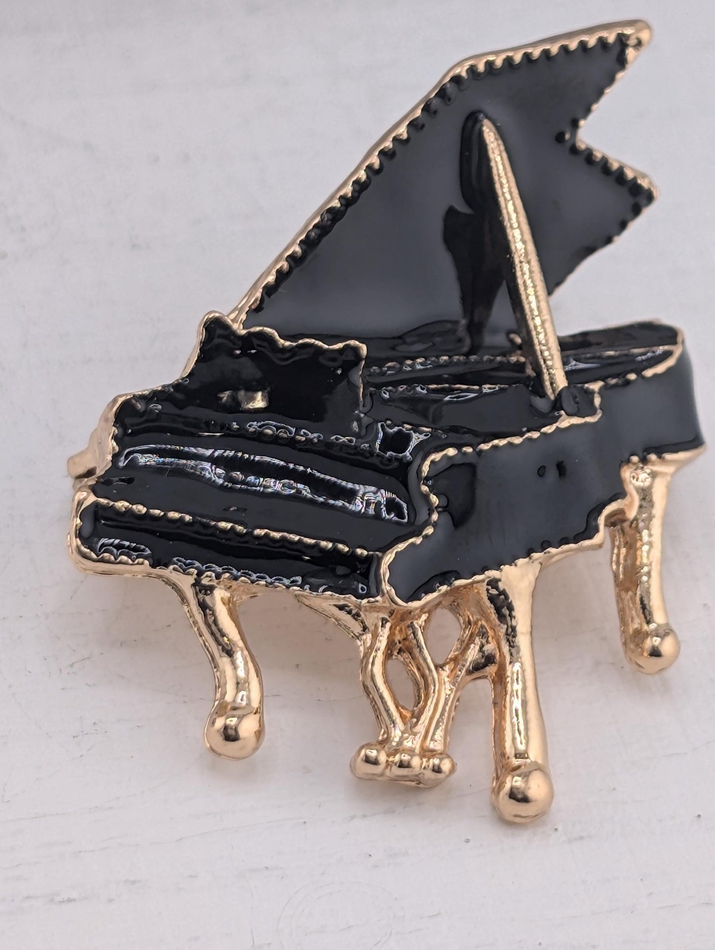 A black and gold piano brooch with a shiny finish, featuring a black piano keyboard and gold accents.