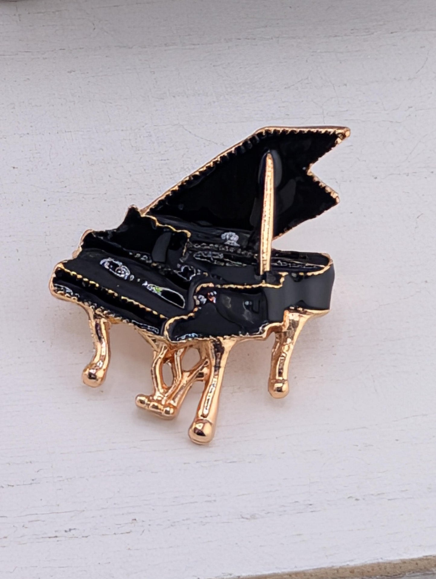 A black and gold piano brooch is displayed against a white background.