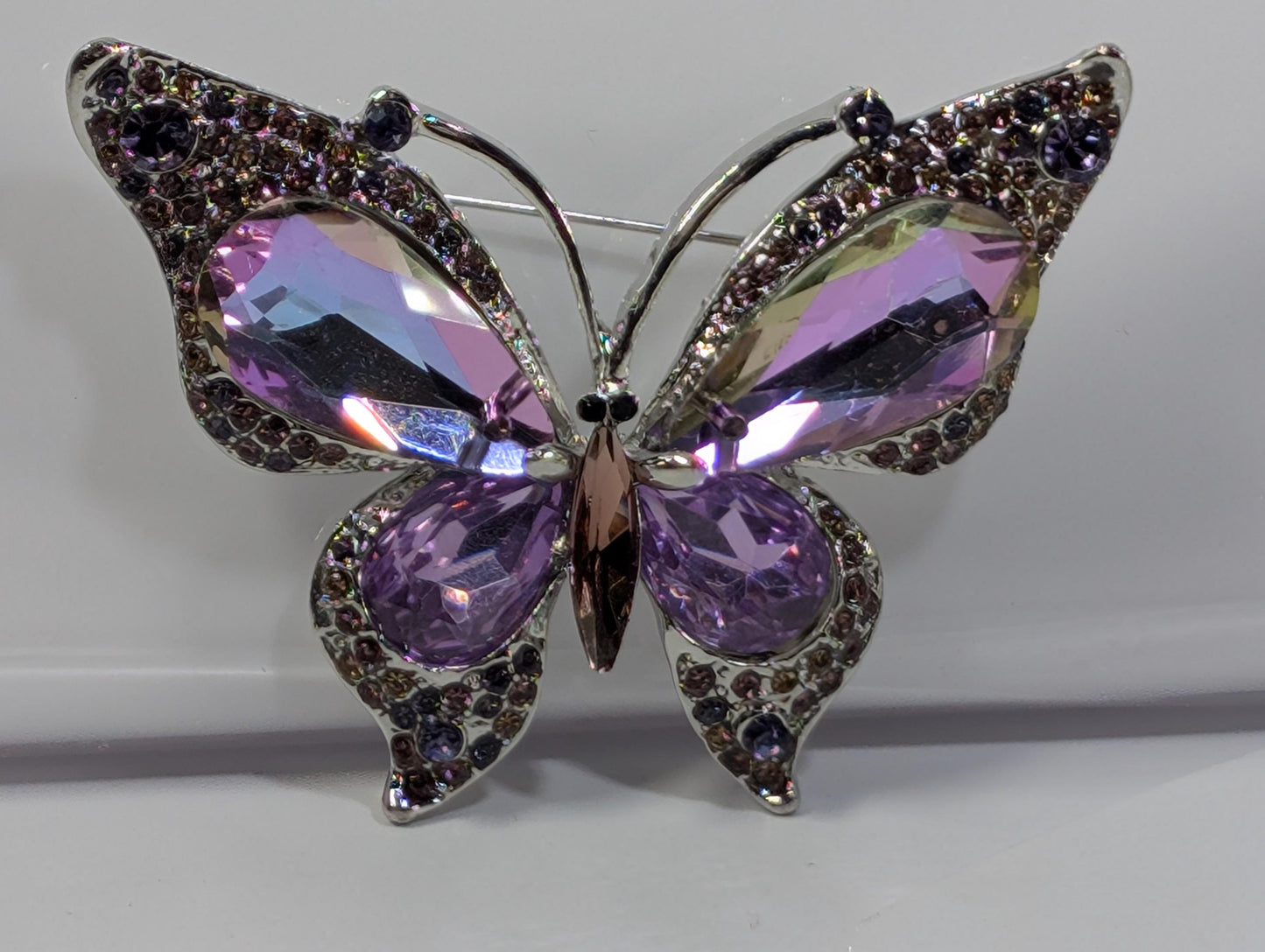 A silver pin in the shape of a butterfly, adorned with purple gemstones.