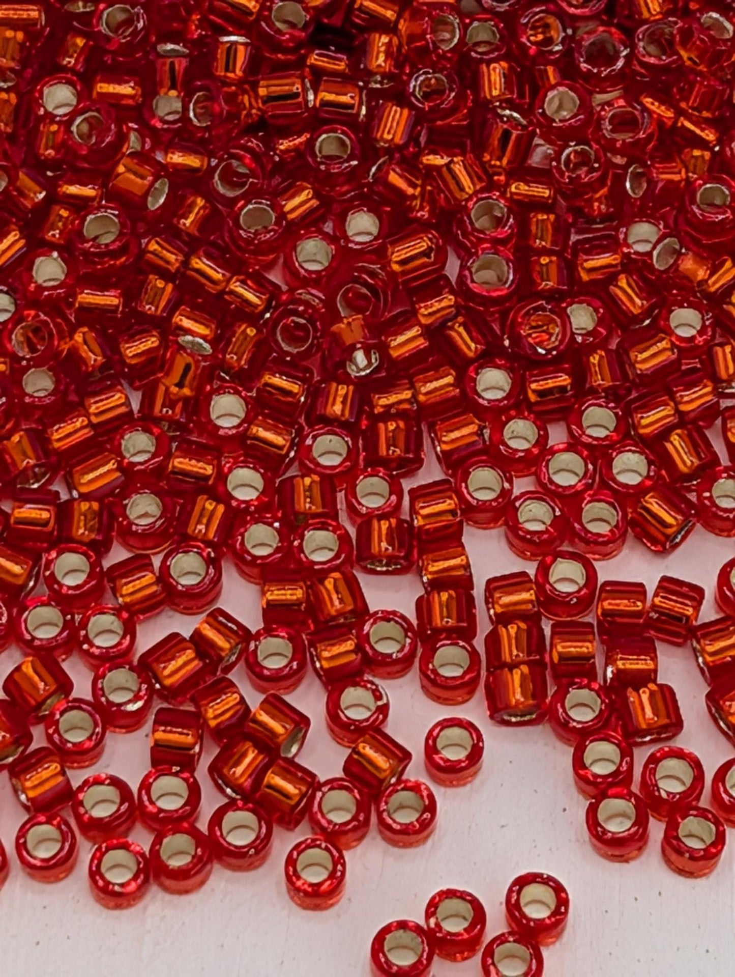 The image is a close-up of numerous red and orange beads scattered across a surface.