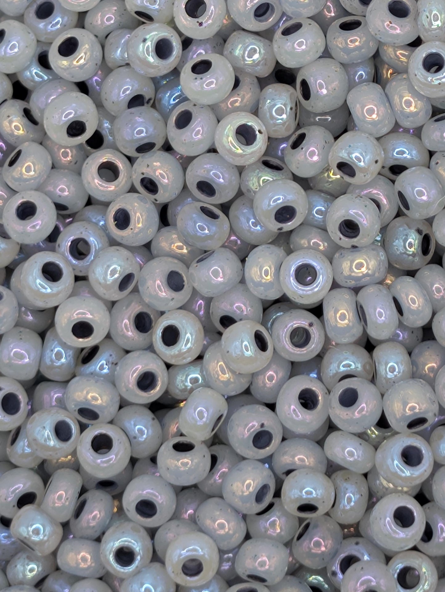 The image is a close-up of numerous small, round beads in various shades of white, with some having a metallic or iridescent appearance.