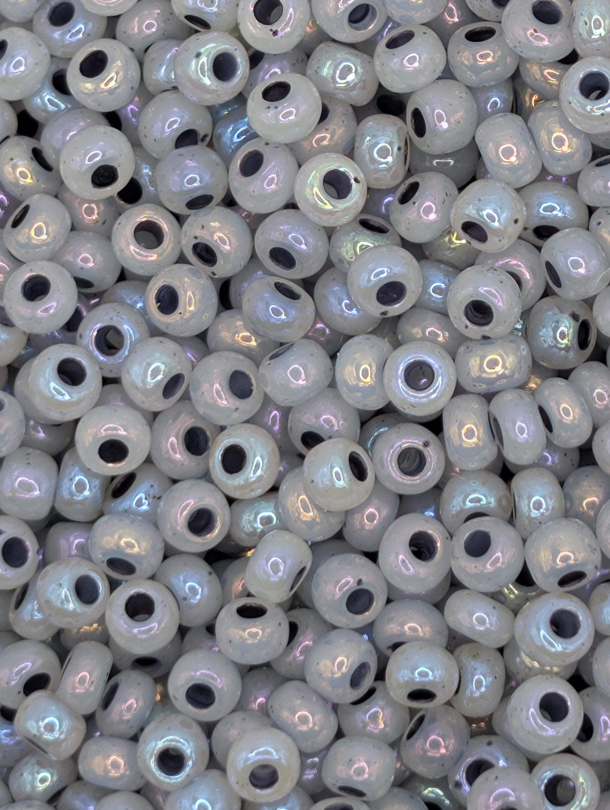 The image is a close-up of numerous small, round beads in various shades of white, with some having a metallic or iridescent appearance.