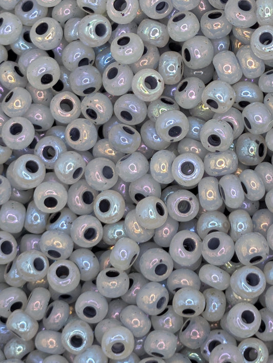 The image is a close-up of numerous small, round beads in various shades of white, with some having a metallic or iridescent appearance.