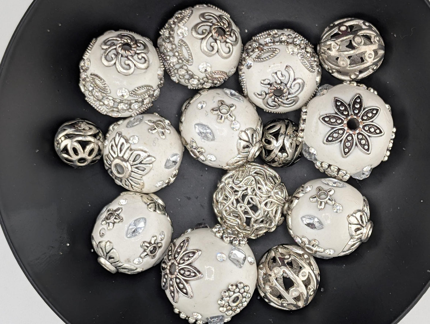 A collection of ornate, silver-colored beads and pendants arranged in a black bowl.