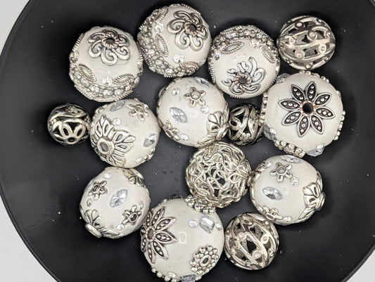 A collection of ornate, silver-colored beads and pendants arranged in a black bowl.