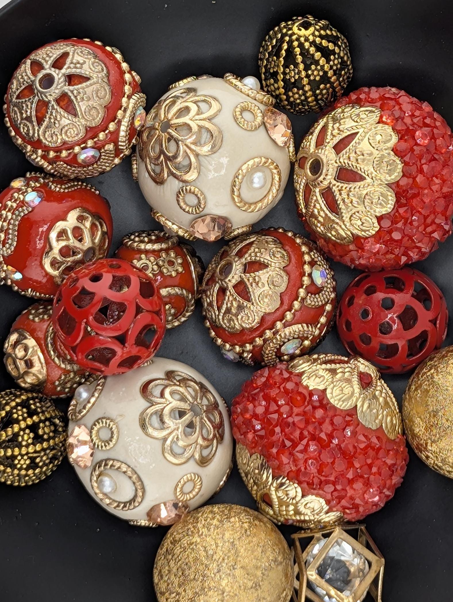 a collection of ornate, decorative objects, including balls, beads, and other embellishments, arranged on a black surface.