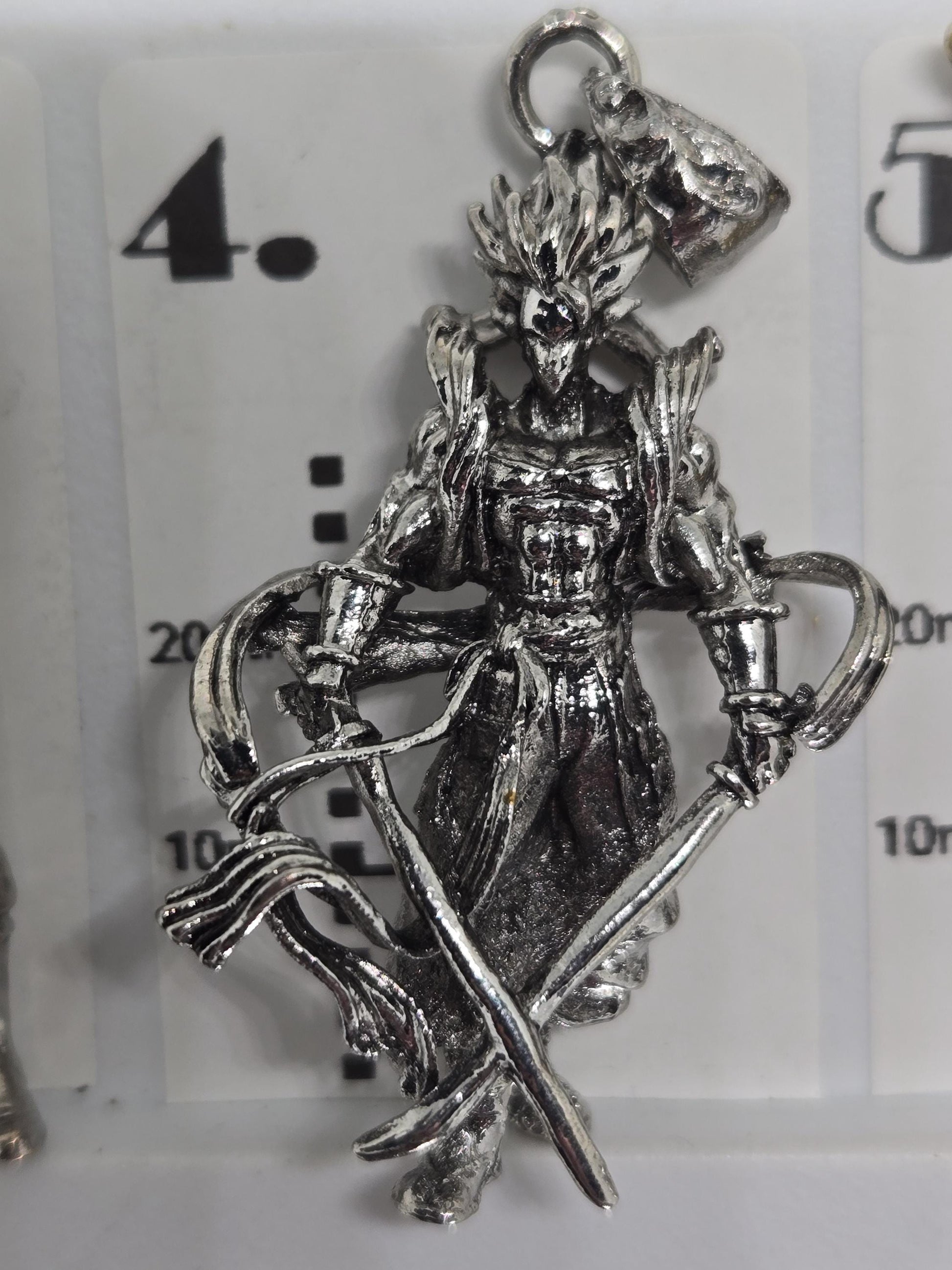 A silver-colored pendant in the shape of a dragon or mythical creature, with intricate details and a metallic sheen.