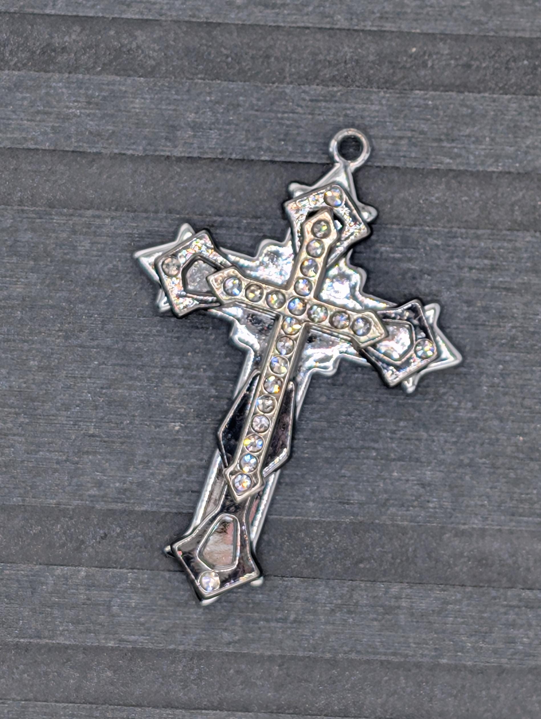 A silver cross pendant with rhinestones or crystals on it, resting on a textured gray surface.