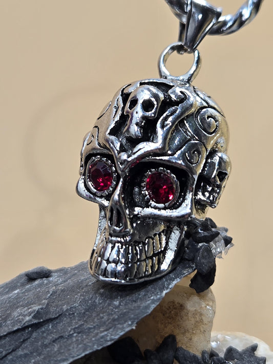 A close-up image of a silver skull pendant with red gemstones, hanging from a chain.