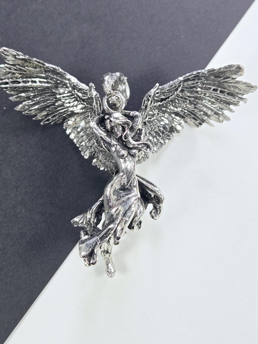 A silver metal sculpture of a winged creature with intricate details and a flowing, dynamic pose.