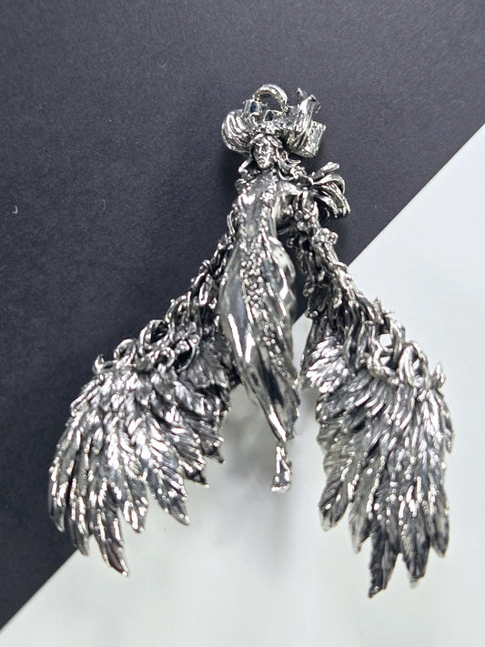 A silver, intricately designed metal sculpture of a winged creature, possibly a dragon or mythical being, is shown against a contrasting background.